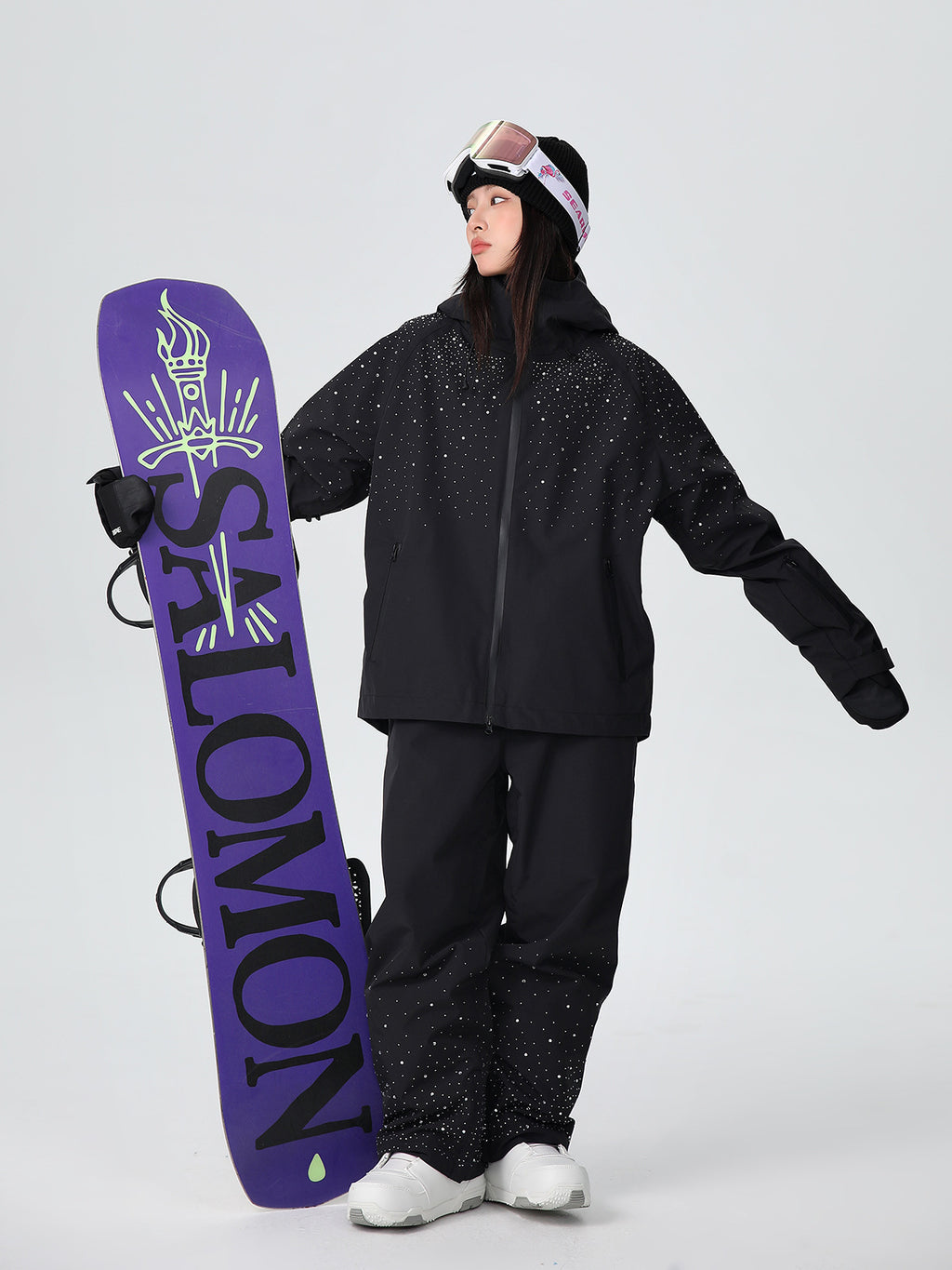 Model wearing the black sparkle ski suit set holding a snowboard