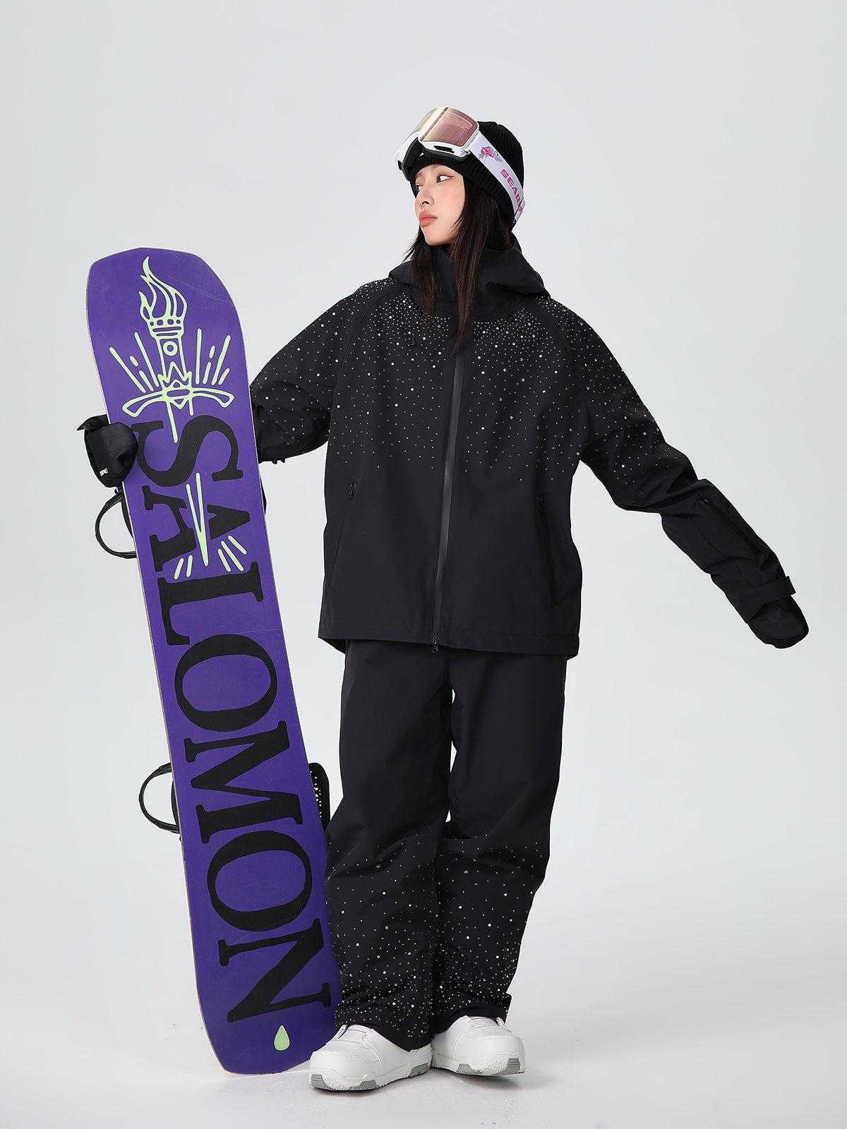 Model wearing the black sparkle ski suit set holding a snowboard