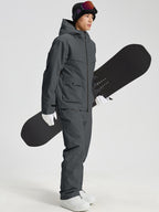 Men's dark grey snowboard jacket and pants set holding a snowboard